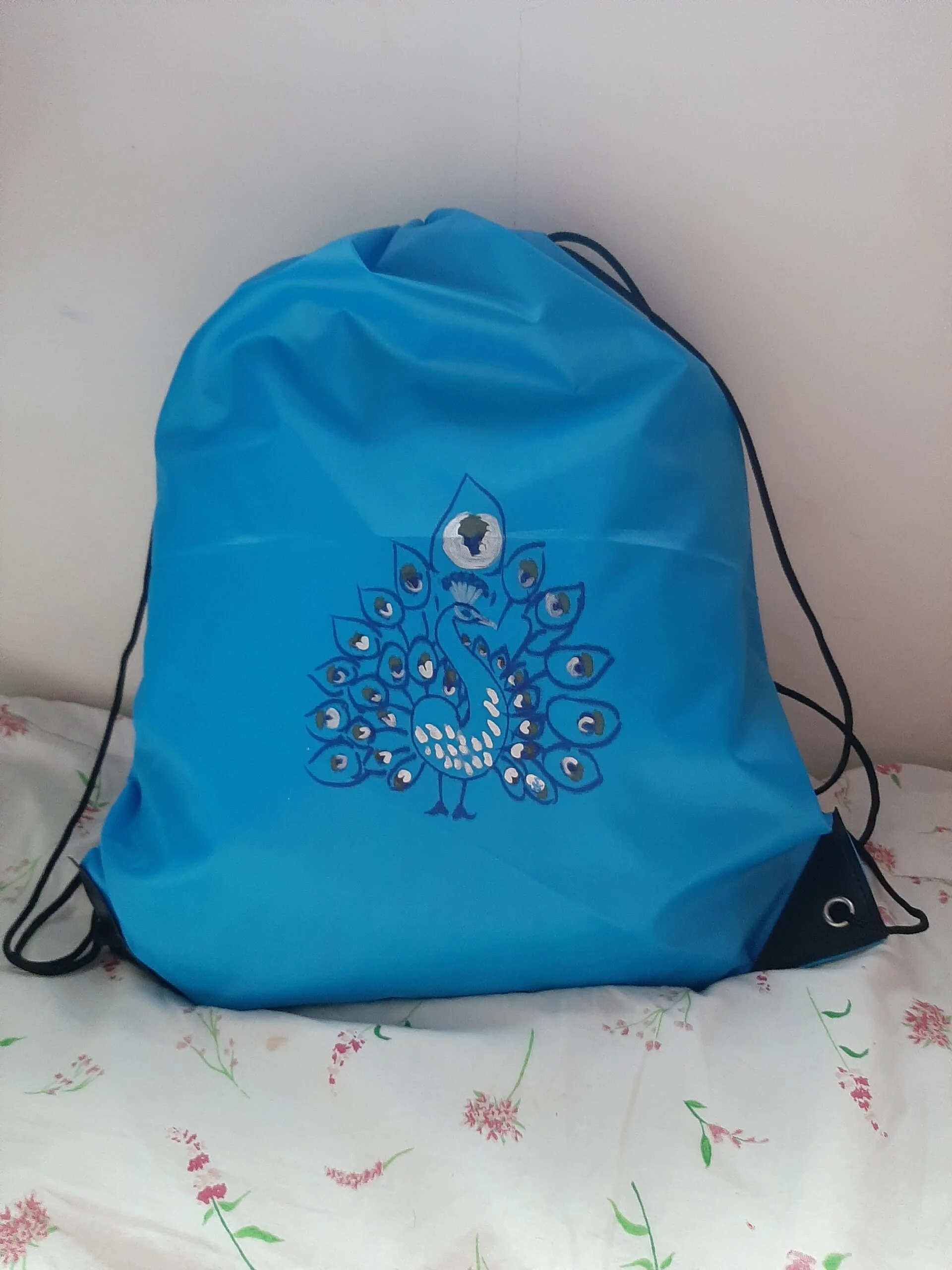 Blue drawstring bag showing hand-painted copyright image of peacock